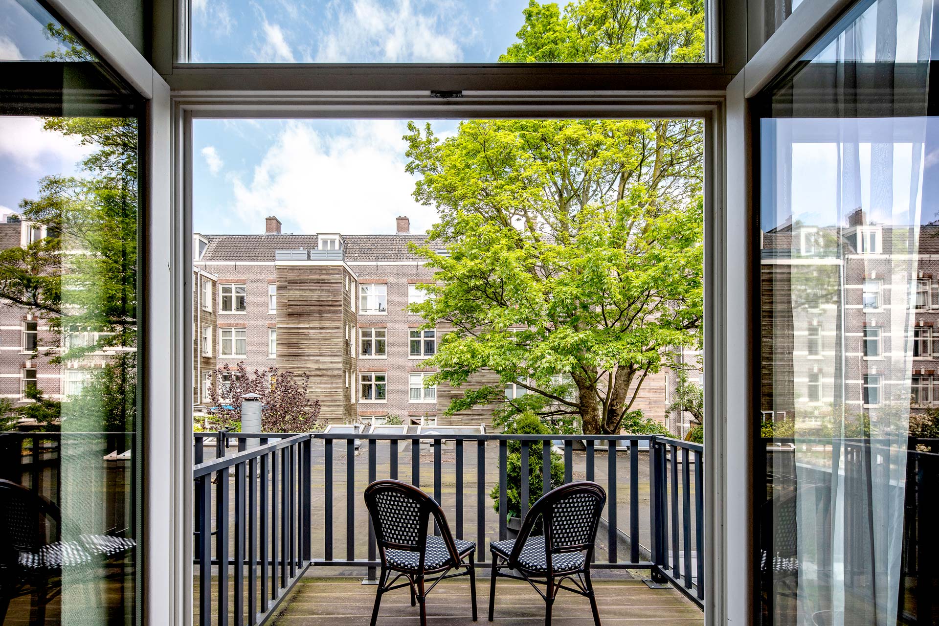 A private balcony with bistro chairs, over the trees on Ceintuurbaan