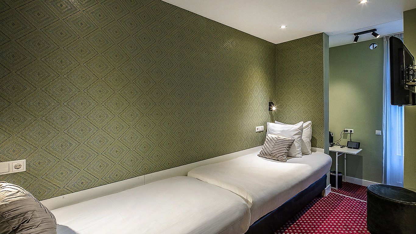 Two single beds end to end against the sage patterned wallpaper, with the desk and window beyond